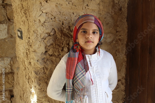 Beautiful young girl wearing white pullover leaning on a mud wall in Siwa in Egypt