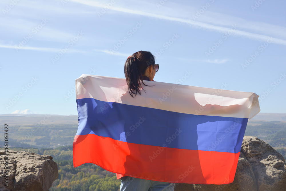 The Russian flag is on the shoulders of a girl standing against the backdrop of the Caucasus mountains. Unity Day in Russia.
