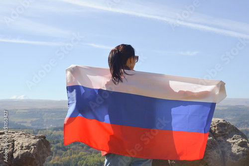 Obraz na płótnie The Russian flag is on the shoulders of a girl standing against the backdrop of the Caucasus mountains. Unity Day in Russia. w salonie