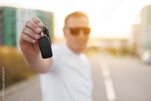 Photography Adult male driver holds new car key with fob outdoors, remote control car alarm systems