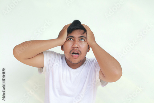 A portrait of an Asian man wearing a white shirt isolated by gray background looks depressed.