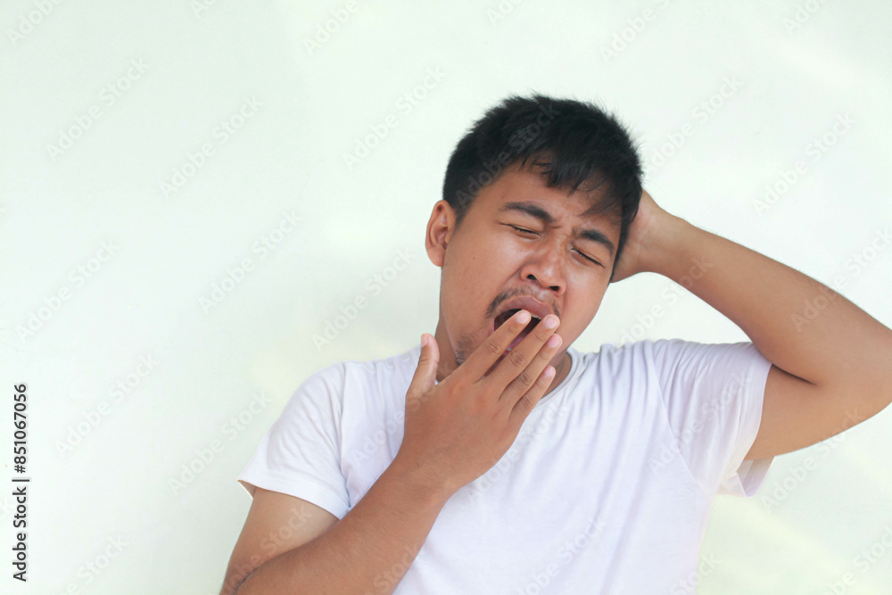 Close up of an asian man with sleepy expression and yawn with messy hair. Wake up concept. With a gray background. Close up of an asian man with sleepy expression and yawn with messy hair. Wake up concept. With a gray background.
