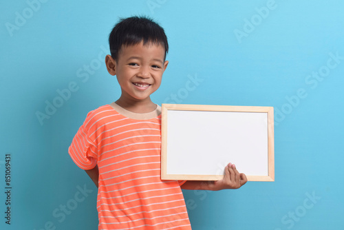 Cute little Asian boy holding a blank board isolated on blue background. Space for text, copy space, mockup banner