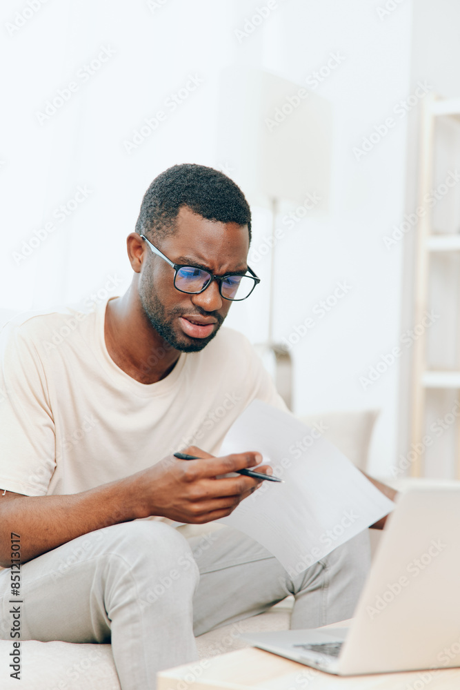 Smiling African American Freelancer Working on Laptop in Modern Home Office The young black man is sitting on a sofa, typing on his computer, surrounded by a comfortable and stylish living room He Smiling African American Freelancer Working on Laptop in Modern Home Office The young black man is sitting on a sofa, typing on his computer, surrounded by a comfortable and stylish living room He