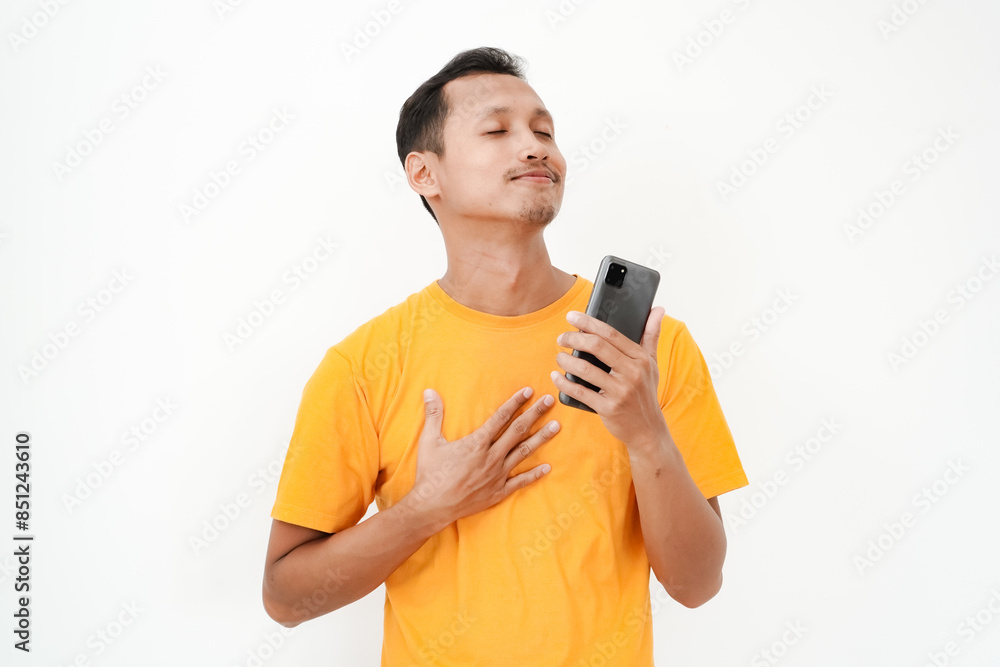 A young man wearing a yellow t-shirt has a happy expression holding a cell phone. With a plain white background A young man wearing a yellow t-shirt has a happy expression holding a cell phone. With a plain white background