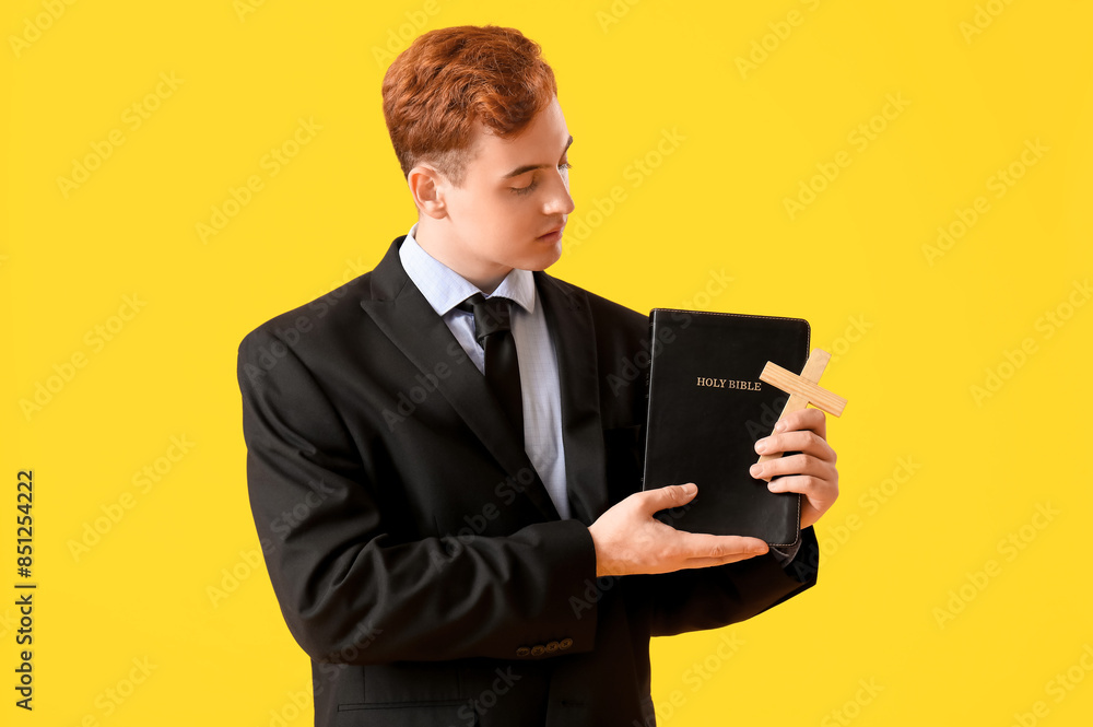 Young redhead man with Bible and wooden cross on yellow background Young redhead man with Bible and wooden cross on yellow background