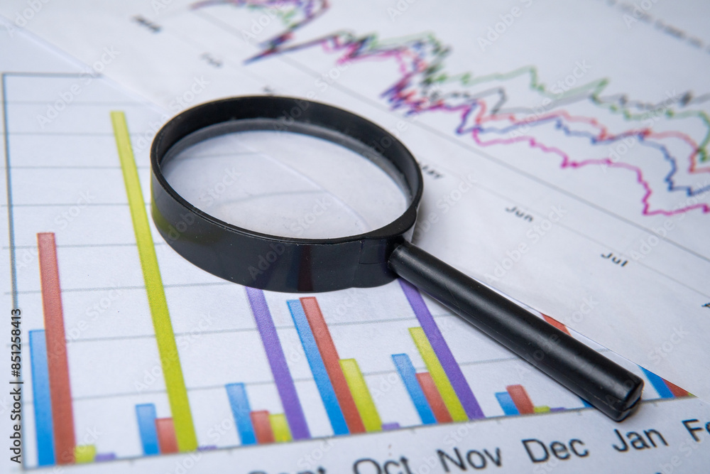 A close-up image of a magnifying glass and graph. Business analysis, due diligence concept. A close-up image of a magnifying glass and graph. Business analysis, due diligence concept.