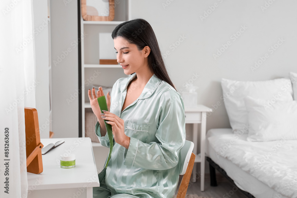 Beautiful young happy woman with plant leaf and jar of aloe vera gel in bedroom Beautiful young happy woman with plant leaf and jar of aloe vera gel in bedroom
