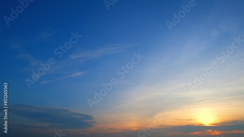 A serene sunrise with a sky that transitions from deep blue to soft yellow and orange hues. The sun is just above the horizon, casting a warm glow and gently illuminating the clouds. 