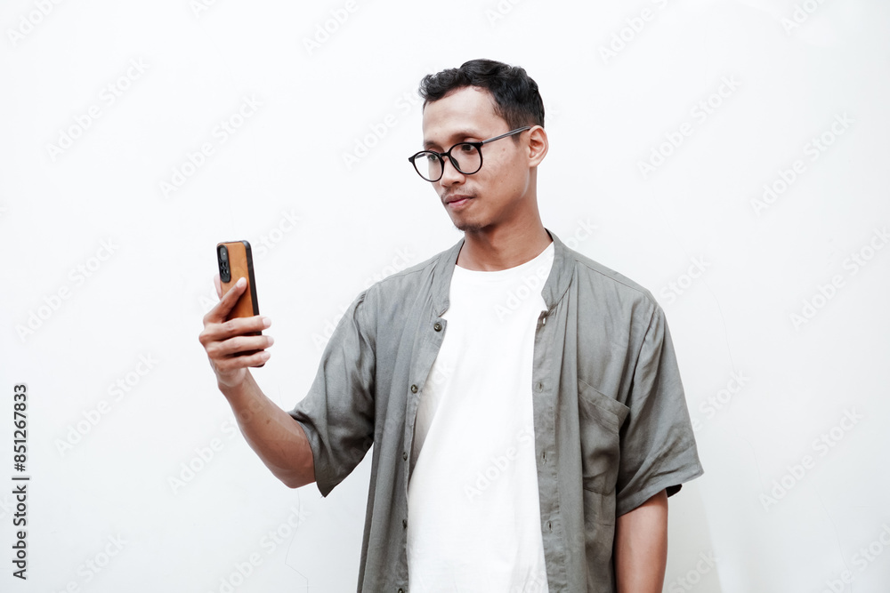 a young man wearing glasses, taking selfies, making video calls, making an expression looking at his cellphone. With a plain white background a young man wearing glasses, taking selfies, making video calls, making an expression looking at his cellphone. With a plain white background