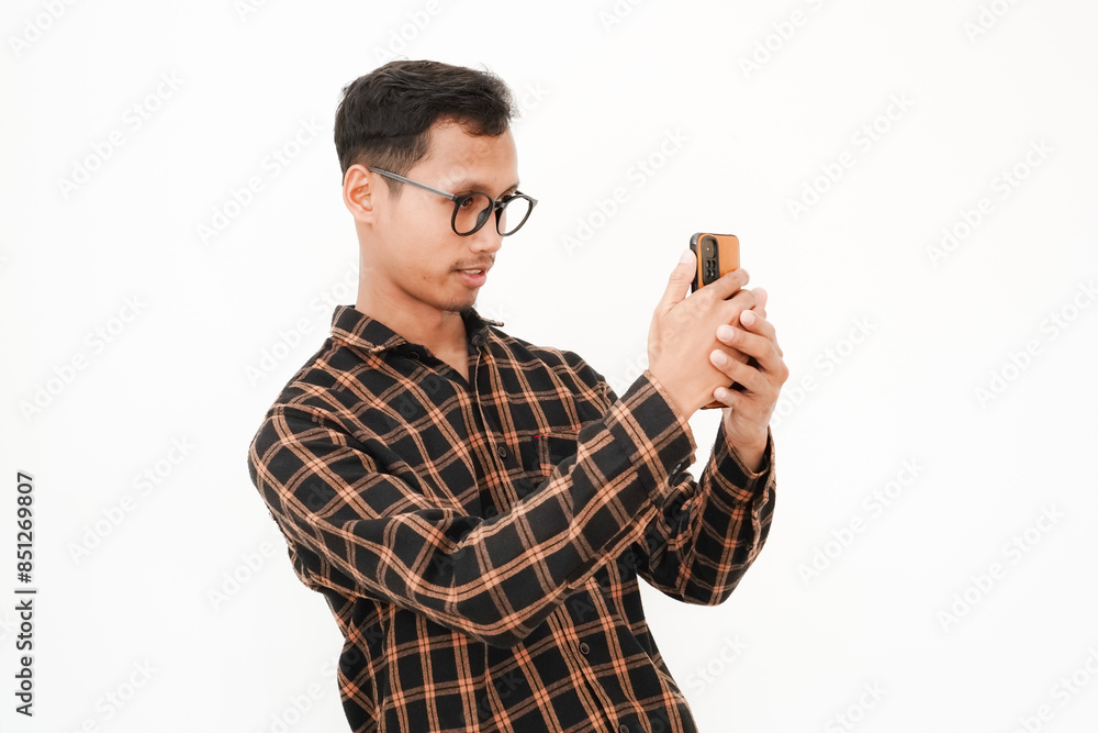 Fototapeta premium a young man wearing a flannel shirt, wearing glasses with a happy expression looking at a cellphone, videocalling, selfie. With a plain white background