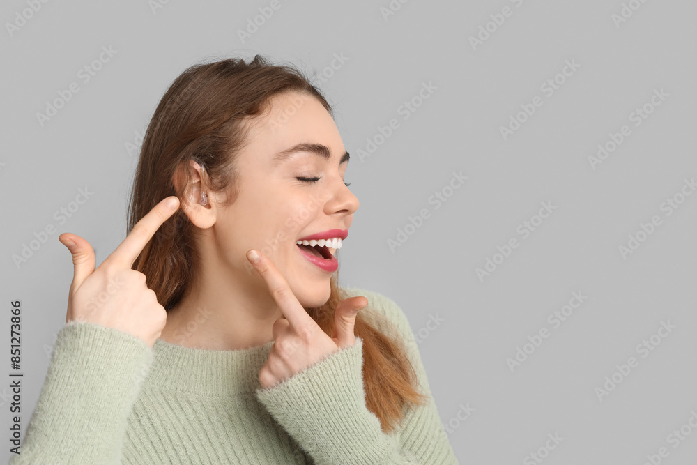 Happy young woman pointing at hearing aid on grey background Happy young woman pointing at hearing aid on grey background