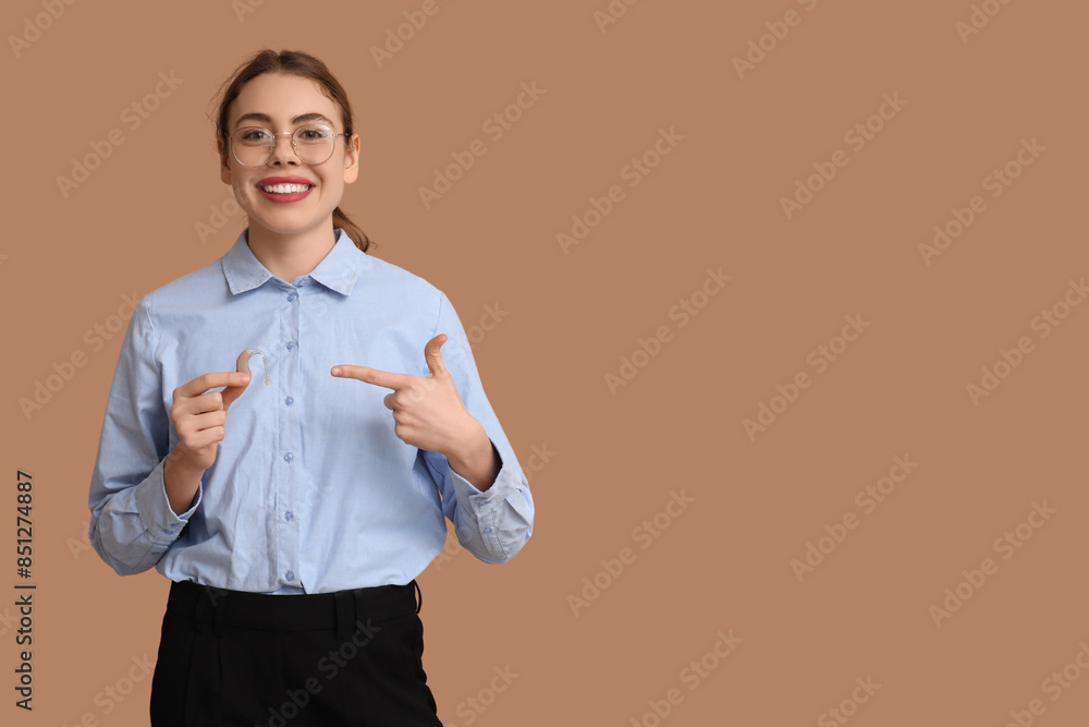 Beautiful young woman pointing at hearing aid on brown background Beautiful young woman pointing at hearing aid on brown background