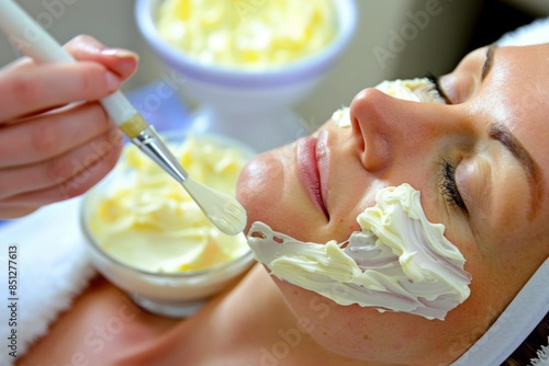 A woman wrapped her head in a white towel, applied a facial mask, massaged her temples with her hands in front of a mirror, a neat and clean modern white room