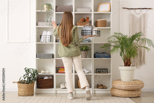 Young woman near shelving unit with clothes and decor at home photo