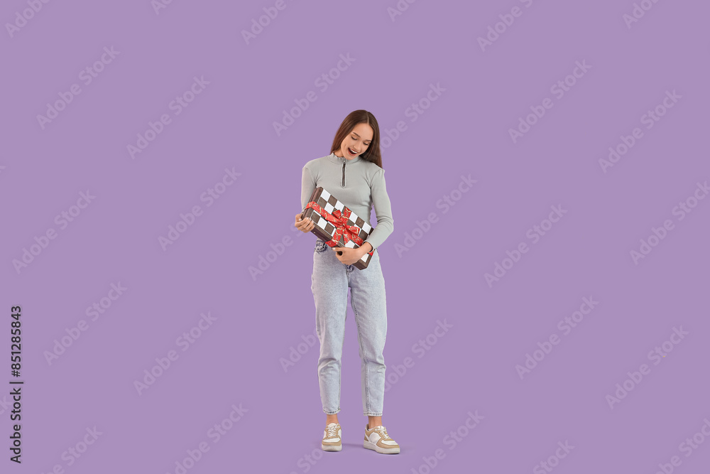 Happy young woman with gift chessboard on lilac background