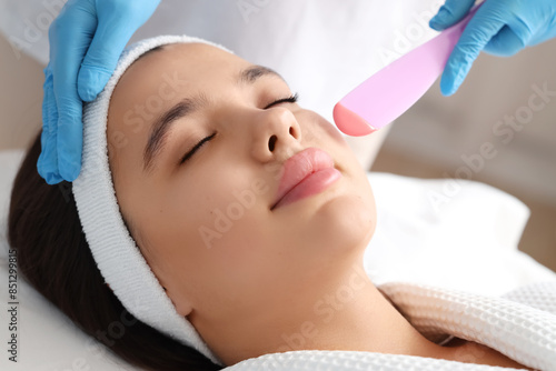 Beautician removing woman's hair on cheek with wax in salon, closeup
