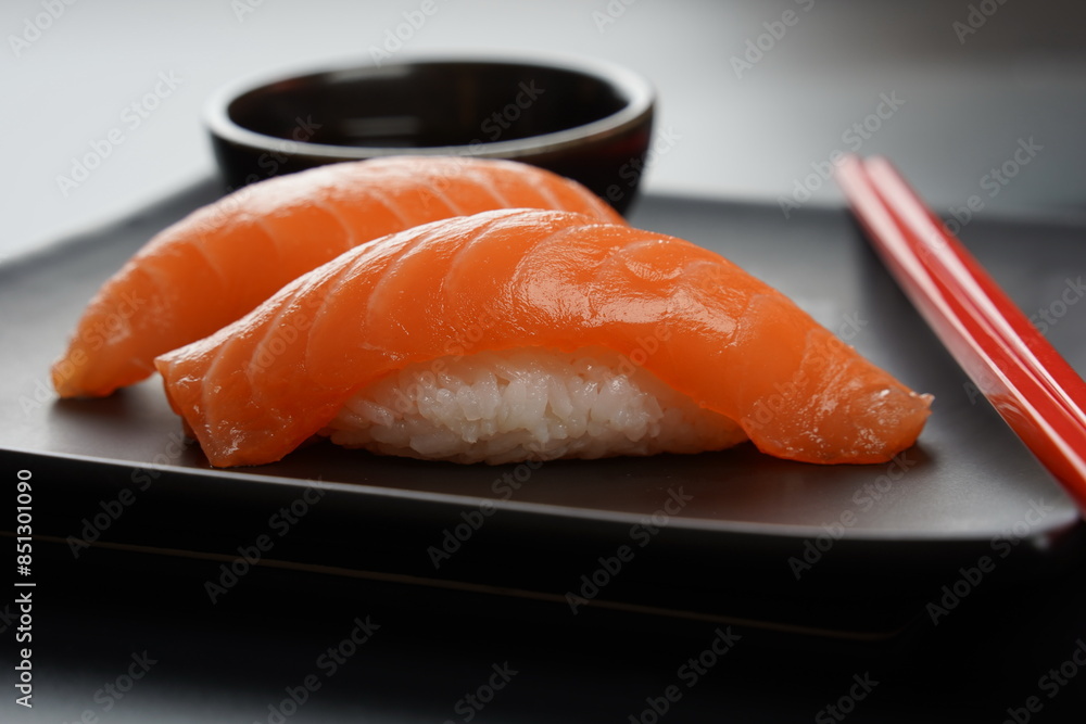 Two pieces of salmon sushi served on a wooden board with soy sauce and chopsticks. Two pieces of salmon sushi served on a wooden board with soy sauce and chopsticks.