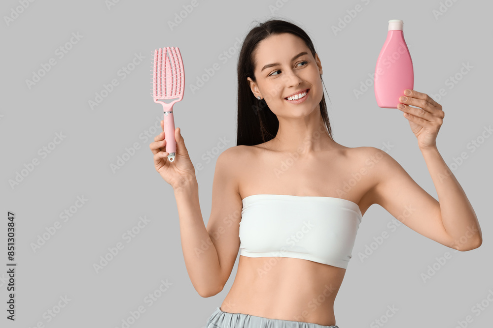 Beautiful young happy woman with bottle of shampoo and hair brush on grey background Beautiful young happy woman with bottle of shampoo and hair brush on grey background