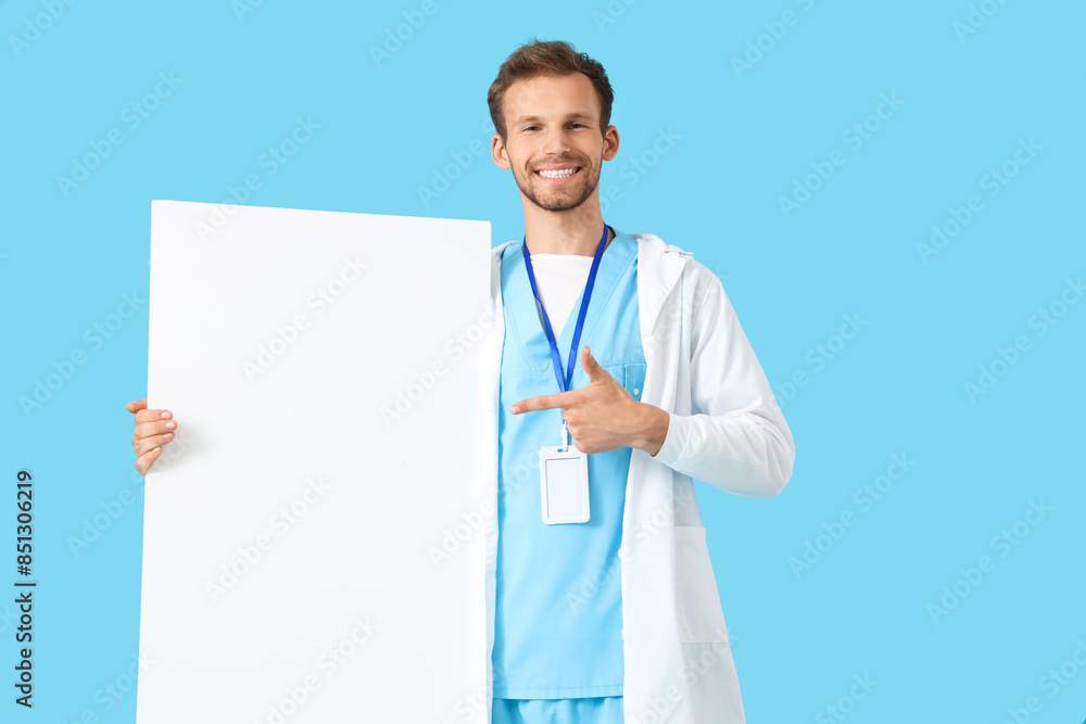Male medical intern pointing at blank poster on blue background Male medical intern pointing at blank poster on blue background