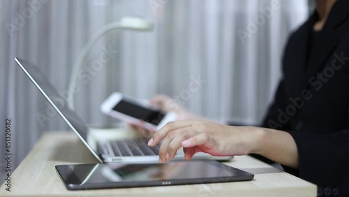 Businessman uses multiple electronic devices simultaneously holding a smartphone in hand The other hand uses a laptop. and interact with the tablet placed on the table. Technology driven environment
