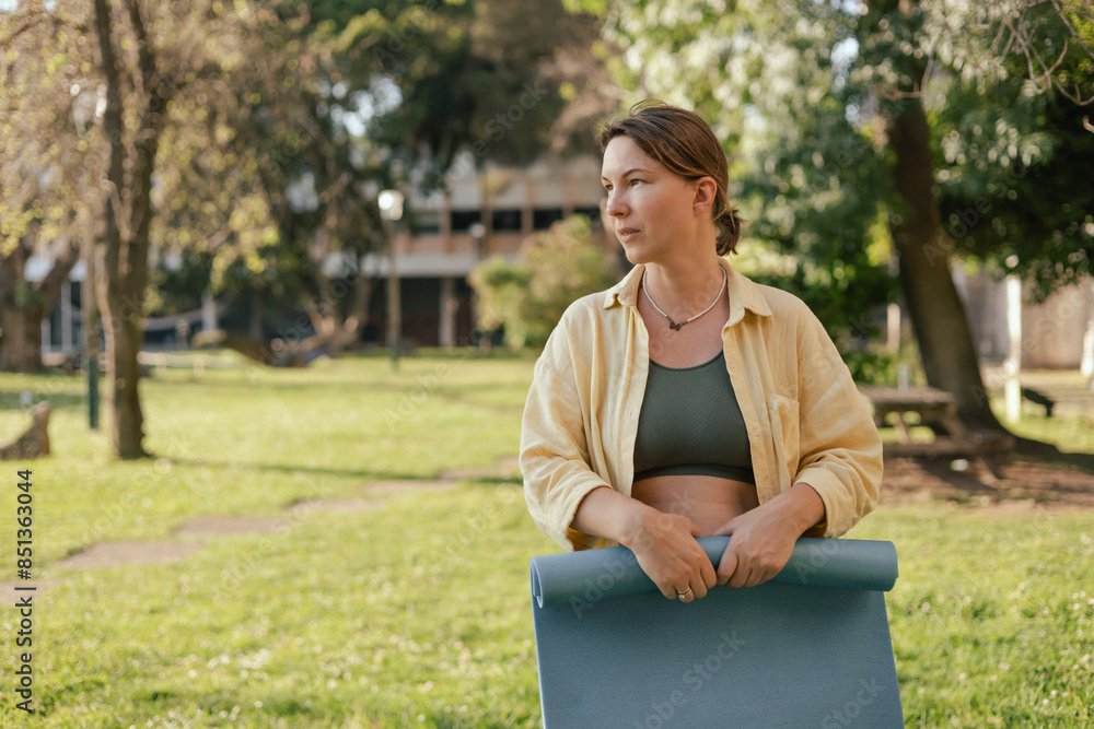 Middle aged woman with yoga mat for practicing yoga in the park. Unity with nature and self sufficient concept Middle aged woman with yoga mat for practicing yoga in the park. Unity with nature and self sufficient concept