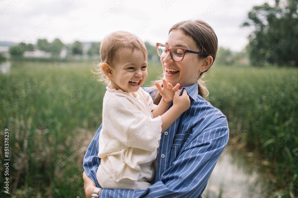 Young mother holding her toddler daughter by the lake having a great time together Young mother holding her toddler daughter by the lake having a great time together