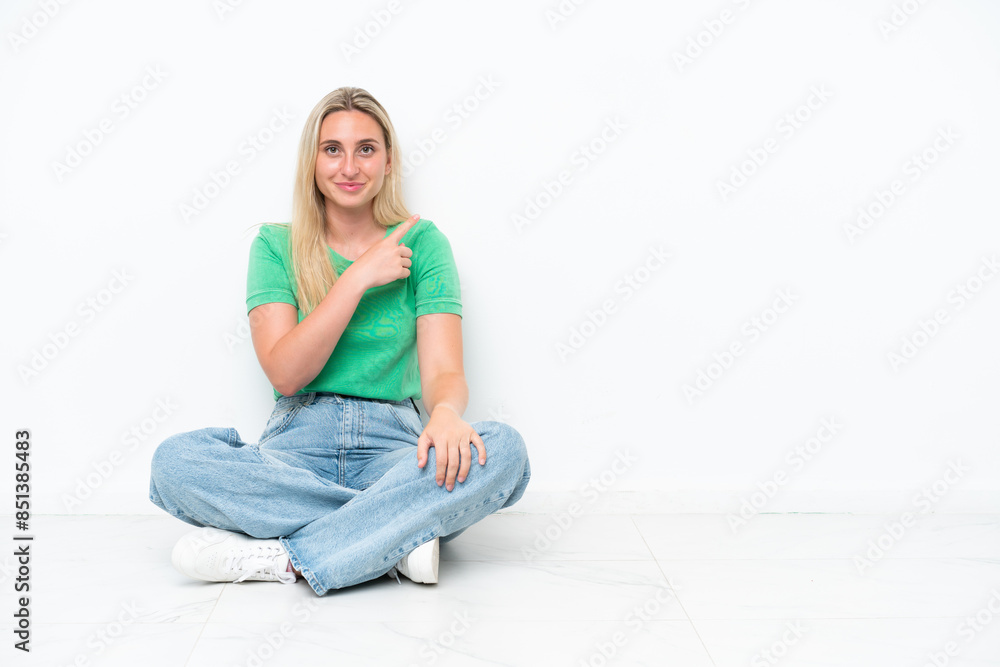 Young caucasian woman sitting on the floor isolated on white background pointing to the side to present a product Young caucasian woman sitting on the floor isolated on white background pointing to the side to present a product