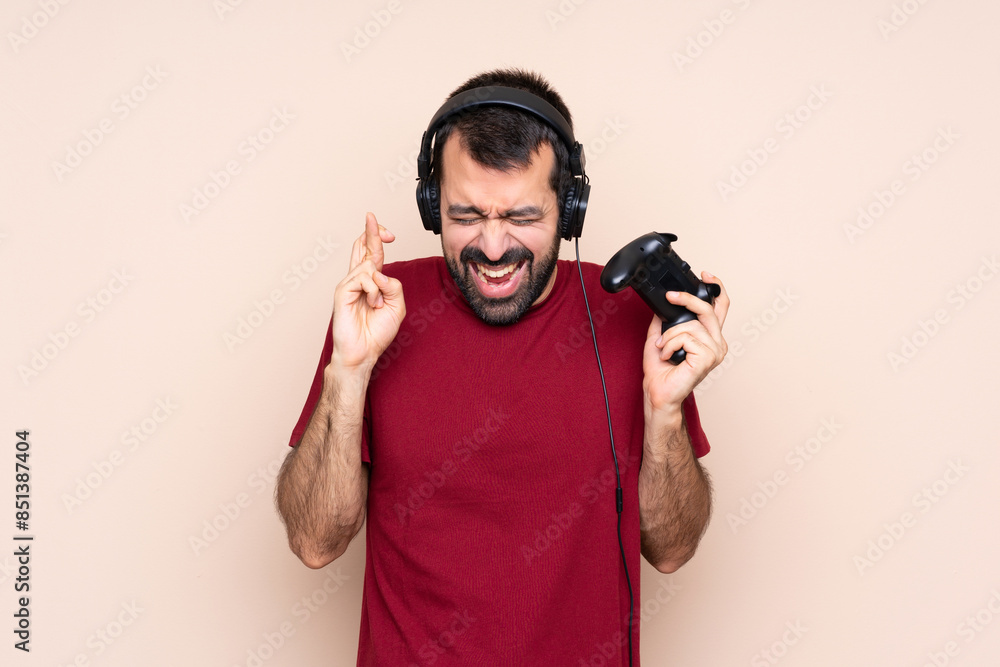 Man playing with a video game controller over isolated wall with fingers crossing Man playing with a video game controller over isolated wall with fingers crossing