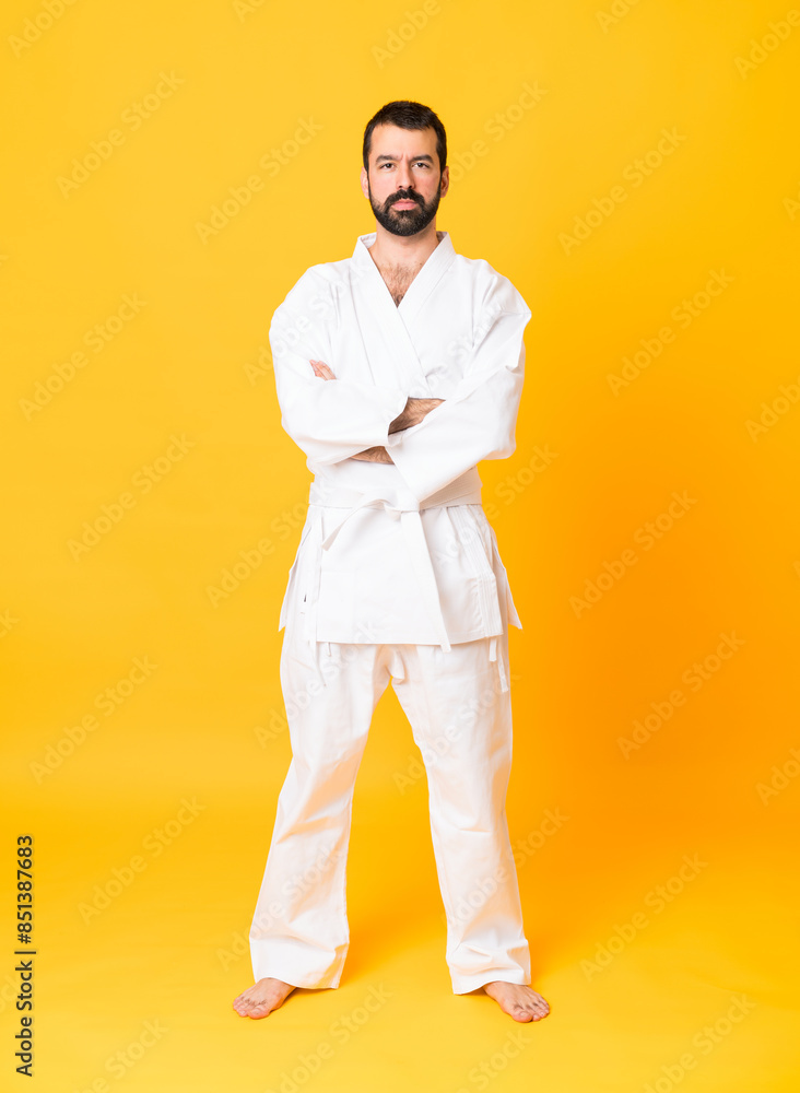 Full-length shot of man over isolated yellow background doing karate keeping the arms crossed Full-length shot of man over isolated yellow background doing karate keeping the arms crossed