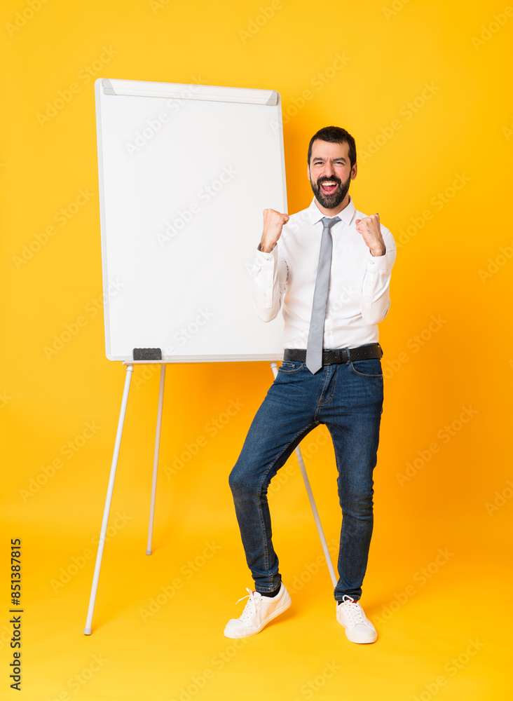 Full-length shot of businessman giving a presentation on white board over isolated yellow background celebrating a victory in winner position Full-length shot of businessman giving a presentation on white board over isolated yellow background celebrating a victory in winner position