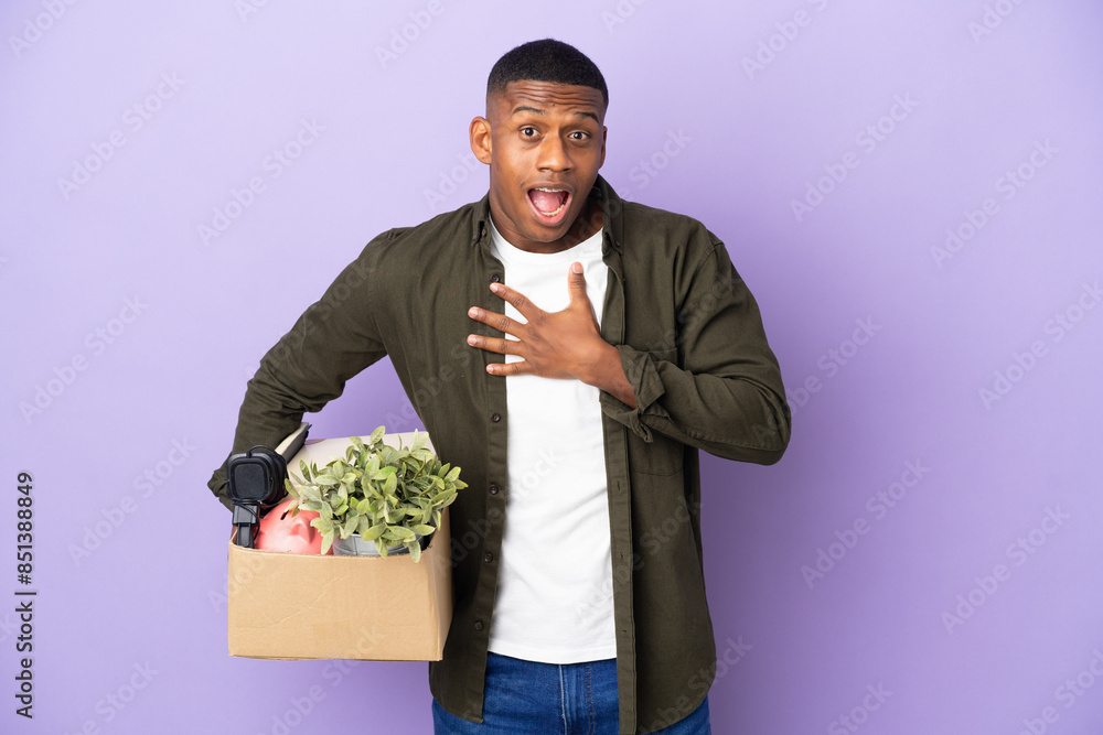 Latin man making a move while picking up a box full of things surprised and shocked while looking right Latin man making a move while picking up a box full of things surprised and shocked while looking right
