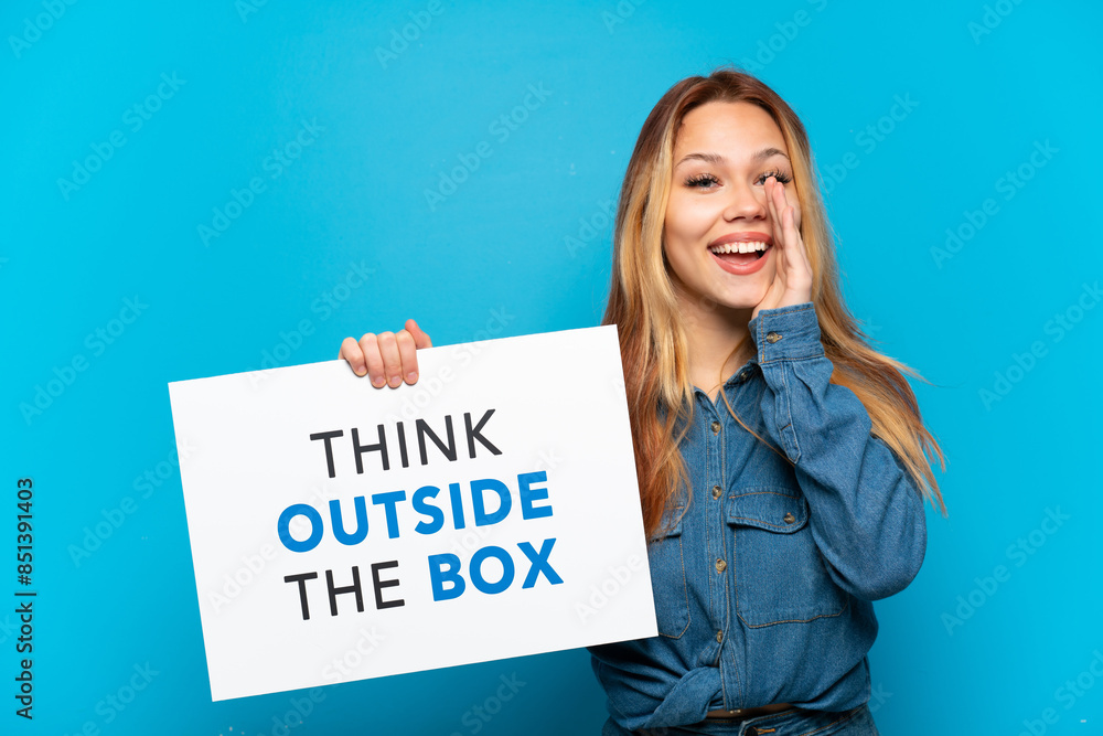 Teenager girl over isolated blue background holding a placard with text Think Outside The Box and shouting Teenager girl over isolated blue background holding a placard with text Think Outside The Box and shouting