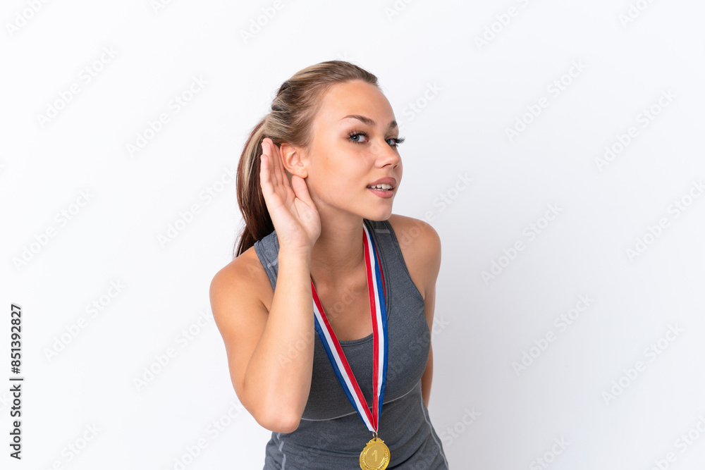 Young sport Russian girl with medals isolated on white background listening to something by putting hand on the ear Young sport Russian girl with medals isolated on white background listening to something by putting hand on the ear