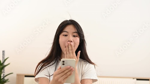 Excited young asian woman reading good news on mobile phone celebrating with yes gesture