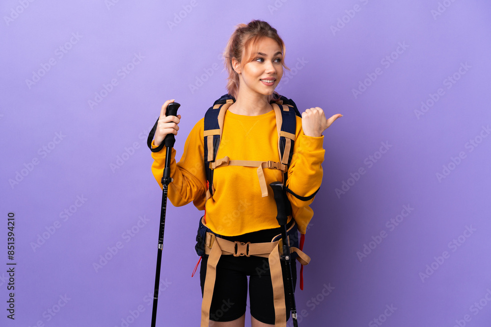 Teenager girl with backpack and trekking poles over isolated purple background pointing to the side to present a product Teenager girl with backpack and trekking poles over isolated purple background pointing to the side to present a product