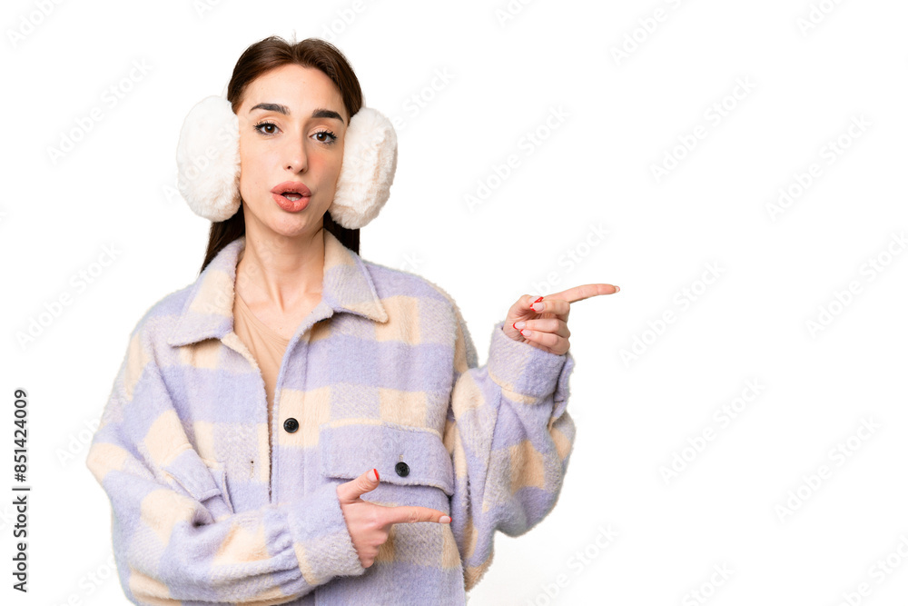 Young caucasian woman wearing winter muffs over isolated chroma key background surprised and pointing side