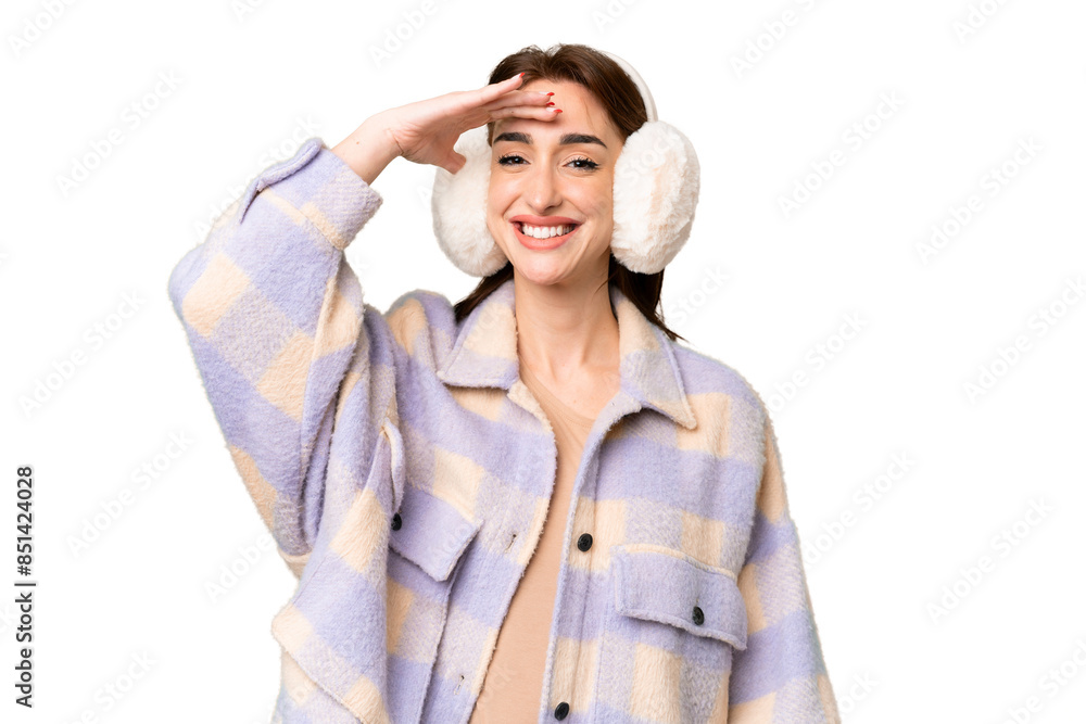 Young caucasian woman wearing winter muffs over isolated chroma key background looking far away with hand to look something Young caucasian woman wearing winter muffs over isolated chroma key background looking far away with hand to look something