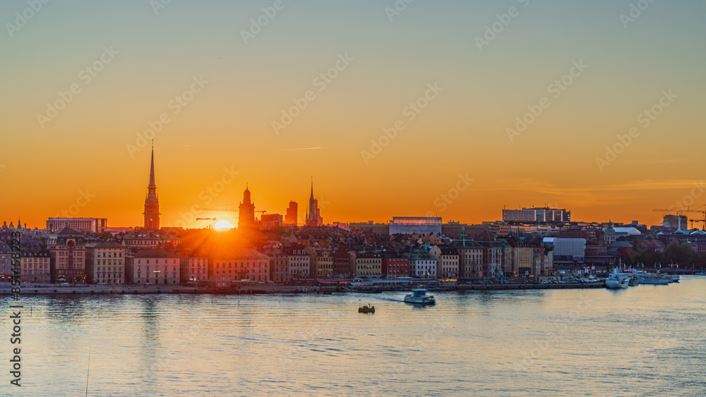 Fototapeta premium Sunset over the old town of Stockholm, skyline of Gamla Stan, silhouette of churches and famous buildings. Boat passing by. Sweden