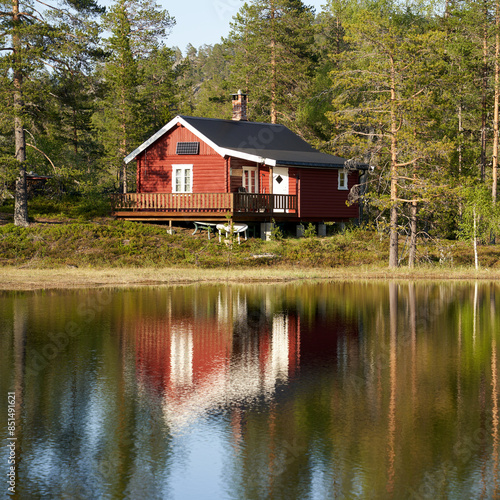 Off-grid, sun-powered, small traditional red wooden cabin by a small lake in Norway during the summer
