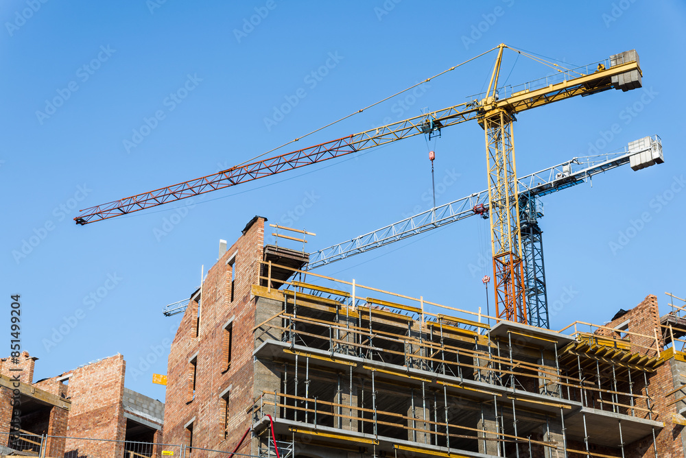 A Pair Of Construction Cranes In Building Site On Blue Sky Background