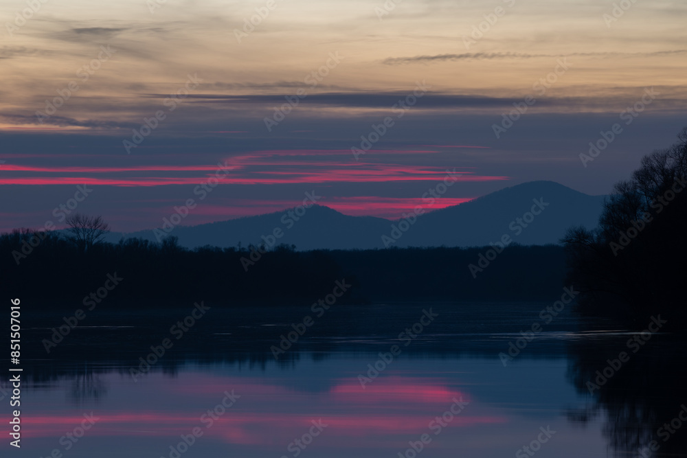 Landscape with mountain reflecting in water at sunset, forest silhouette and bright red glow in clouds Landscape with mountain reflecting in water at sunset, forest silhouette and bright red glow in clouds