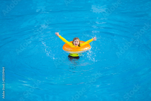 Kid playing with inflatable ring in swimming pool on summer day. Little kid swimming in pool. Kid in swimming pool relax and swim on inflatable ring. Summer vacation concept. Summer vacation. © Volodymyr