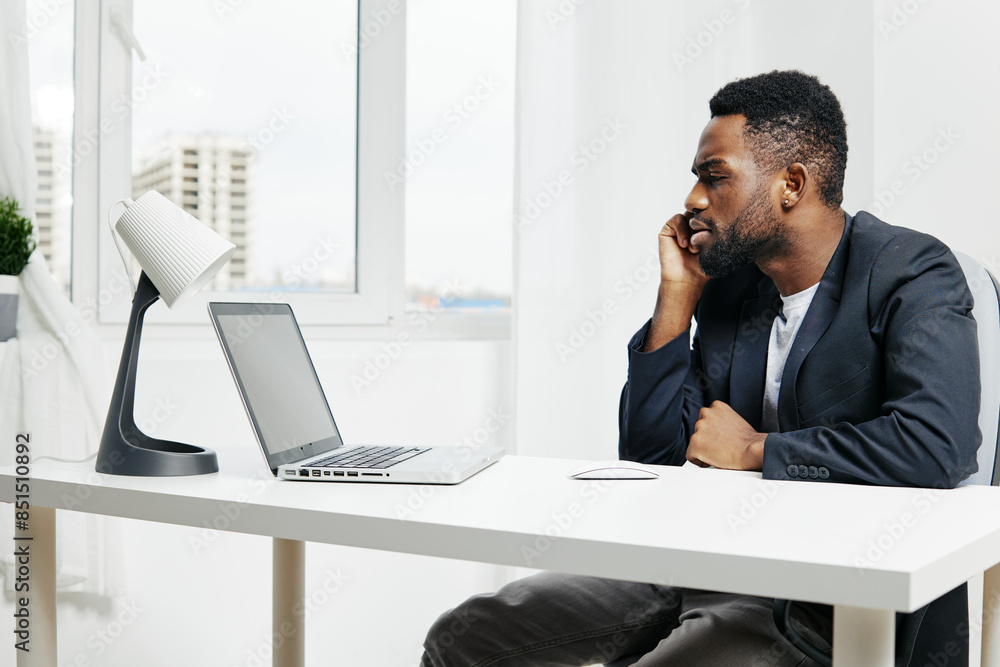 African american man multitasking at desk with laptop, engaging in a phone call, focused on professional work African american man multitasking at desk with laptop, engaging in a phone call, focused on professional work