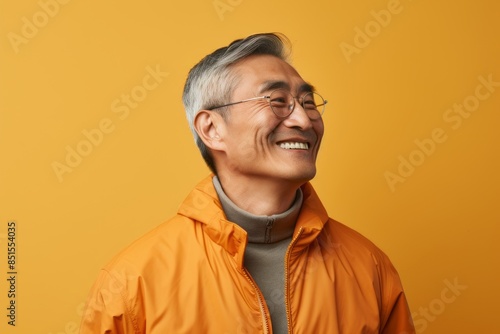 Portrait of a satisfied asian man in his 60s dressed in a water-resistant gilet isolated in light wood minimalistic setup © CogniLens