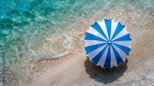 Aerial view of a blue and white beach umbrella on sandy shore with clear turquoise water, perfect summer vacation scene. photo
