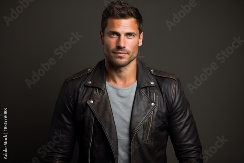 Portrait of a merry man in his 30s sporting a classic leather jacket isolated on plain cyclorama studio wall © CogniLens