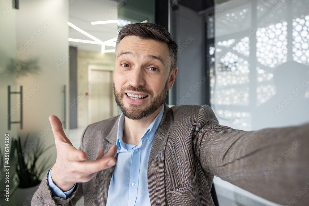 Businessman in a modern office making a video call, smiling and engaging with the camera while gesturing Businessman in a modern office making a video call, smiling and engaging with the camera while gesturing
