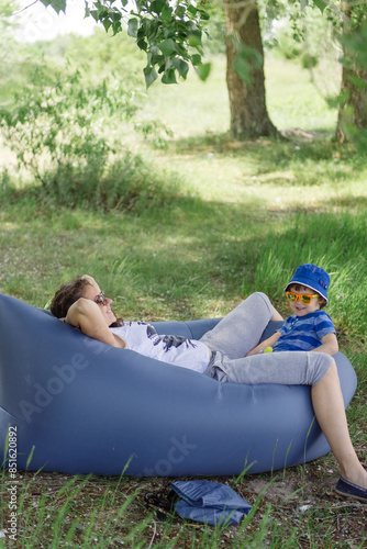 Mom and her child are playing on an inflatable couch under a tree in nature in the spring.