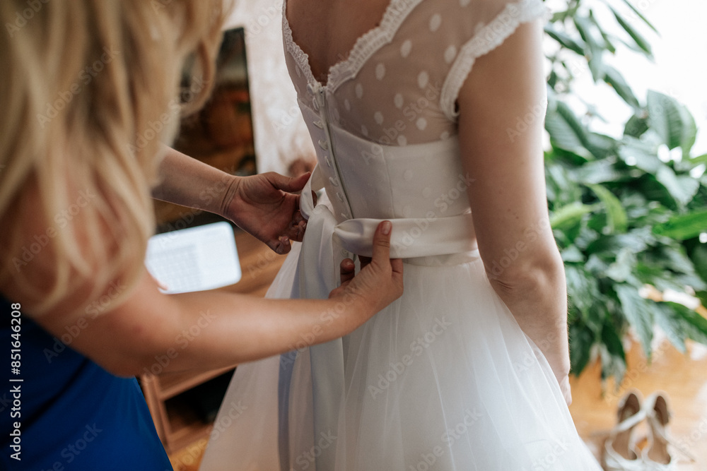A bride or bridesmaid carefully adjusts the laces or buttons of a wedding dress, highlighting the detailed preparations and anticipation before the ceremony. A bride or bridesmaid carefully adjusts the laces or buttons of a wedding dress, highlighting the detailed preparations and anticipation before the ceremony.